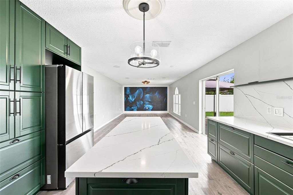 A kitchen features a long white quartz island, green cabinetry, and a blue floral accent wall — 10464 FLY FISHING STREET, RIVERVIEW, FL