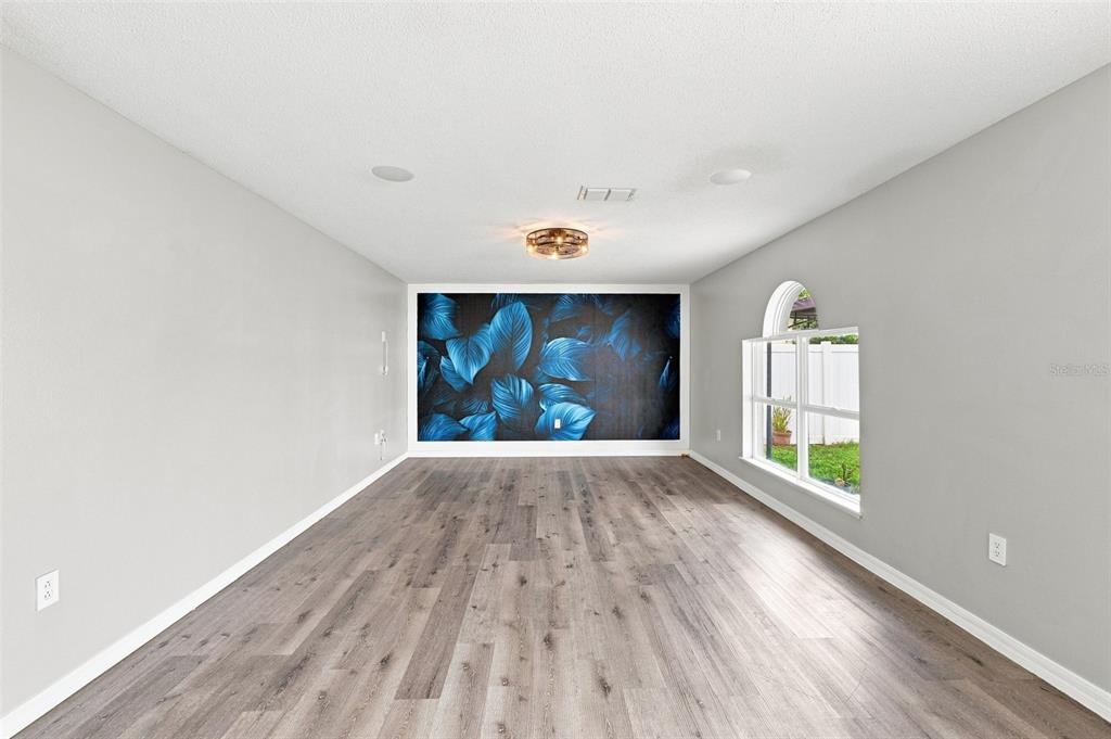An empty room features gray walls, wood-look flooring, a central light fixture, and a leaf-patterned accent wall — 10464 FLY FISHING STREET, RIVERVIEW, FL