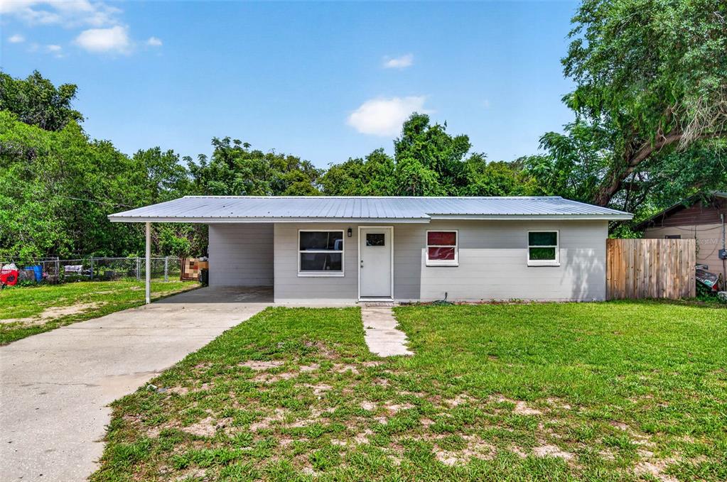 A single-story gray house with a metal roof, a carport, and a grassy front yard — 14002 MORGAN ST, DADE CITY, FL