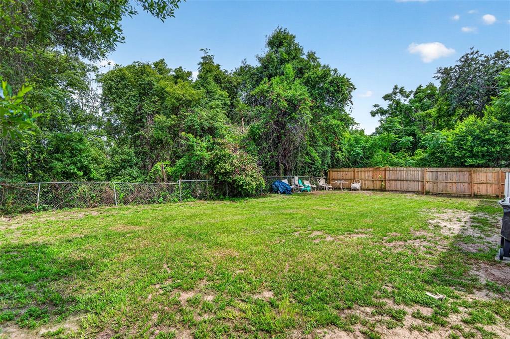 A grassy backyard features a wooden fence, a chain-link fence, and dense surrounding trees — 14002 MORGAN ST, DADE CITY, FL
