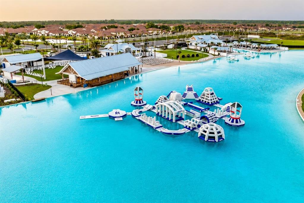An aerial view shows a large turquoise lagoon with an inflatable water park obstacle course — 8668 SALMAR LOOP, PARRISH, FL