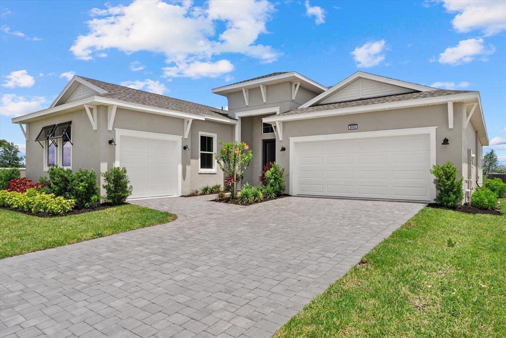 A single-story house with a gray stucco exterior, two garage doors, and a paver driveway — 8668 SALMAR LOOP, PARRISH, FL