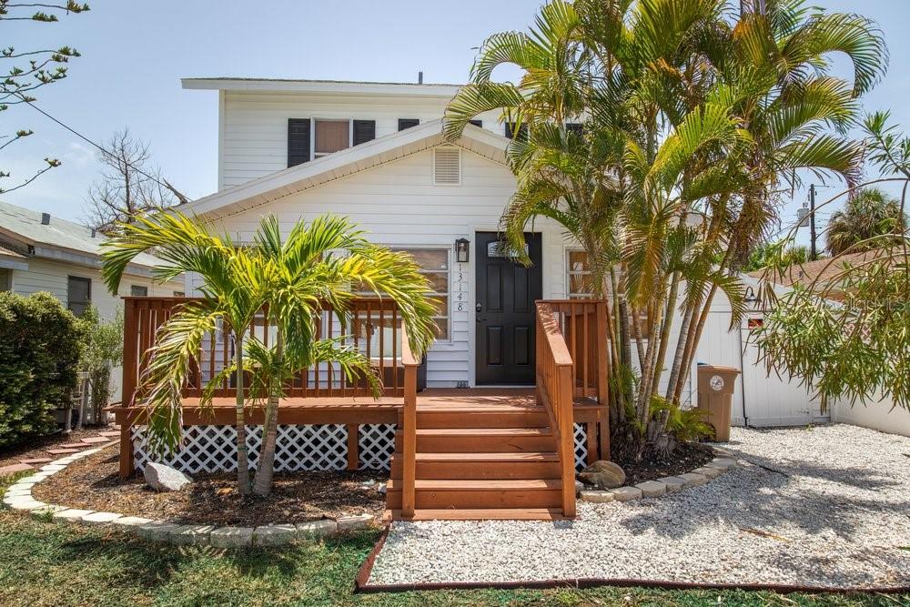 A white two-story house features a wooden front deck, stairs, and palm trees — 13148 3RD STREET E, MADEIRA BEACH, FL