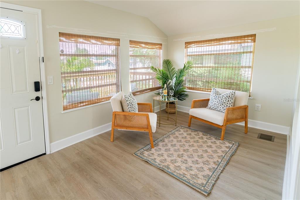 A bright sunroom features light wood flooring, two rattan chairs, a small table, and windows — 13148 3RD STREET E, MADEIRA BEACH, FL