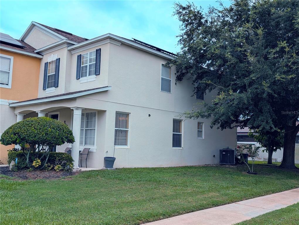 A two-story beige house with a front porch, solar panels, and a large tree — 4664 CAVERNS DRIVE, KISSIMMEE, FL