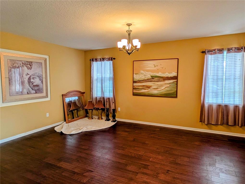 A dining room features yellow walls, dark hardwood floors, a chandelier, and two windows — 4664 CAVERNS DRIVE, KISSIMMEE, FL
