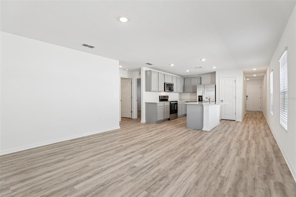 An open-concept kitchen and living area feature light wood-look flooring and grey cabinetry — 3328 WHITE INDIGO ROAD, WINTER HAVEN, FL