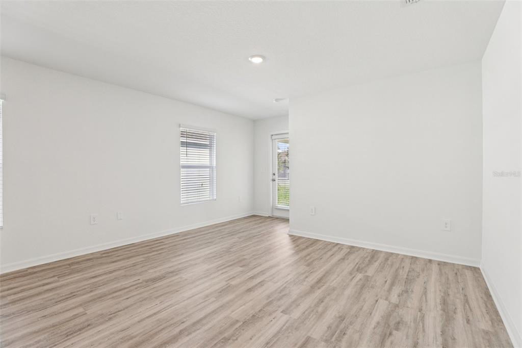 An empty room features white walls, light wood-look flooring, a window, and a glass door — 3328 WHITE INDIGO ROAD, WINTER HAVEN, FL