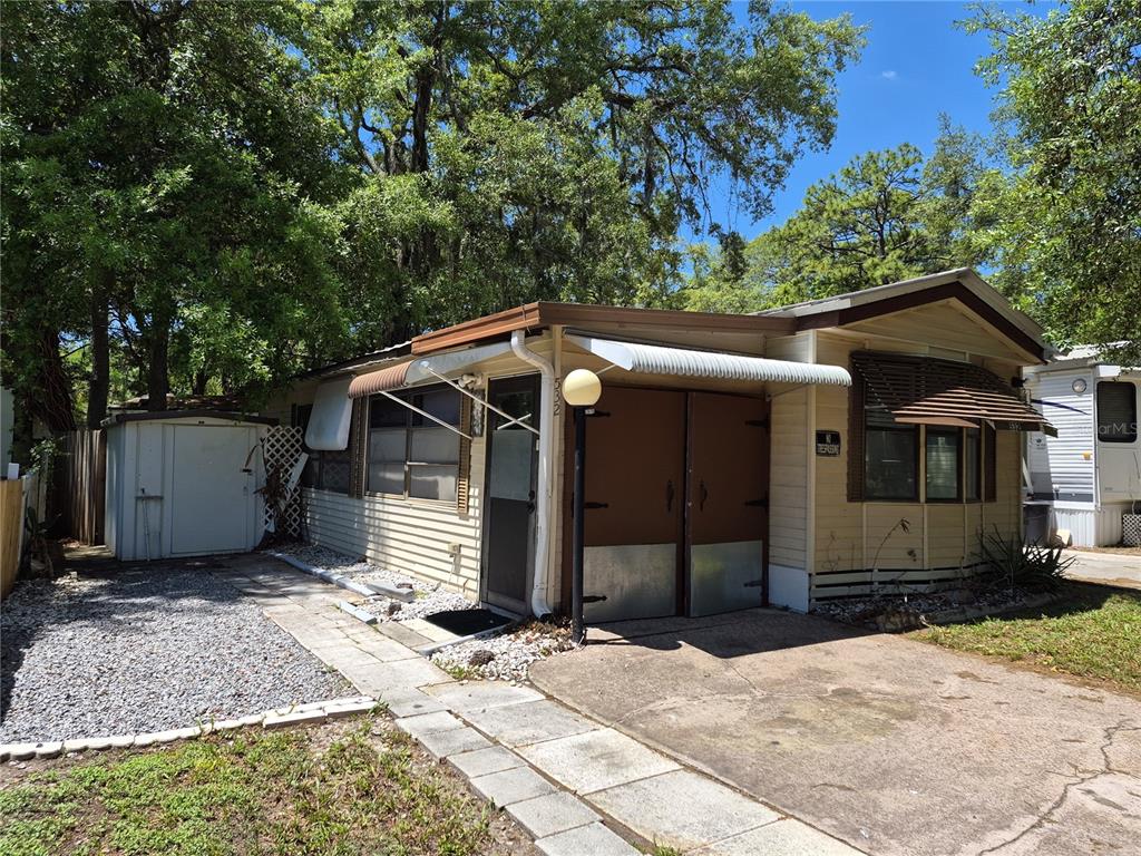 A single-story mobile home with tan siding, a gravel driveway, and a small storage shed — 3000 CLARCONA ROAD UNIT 532, APOPKA, FL