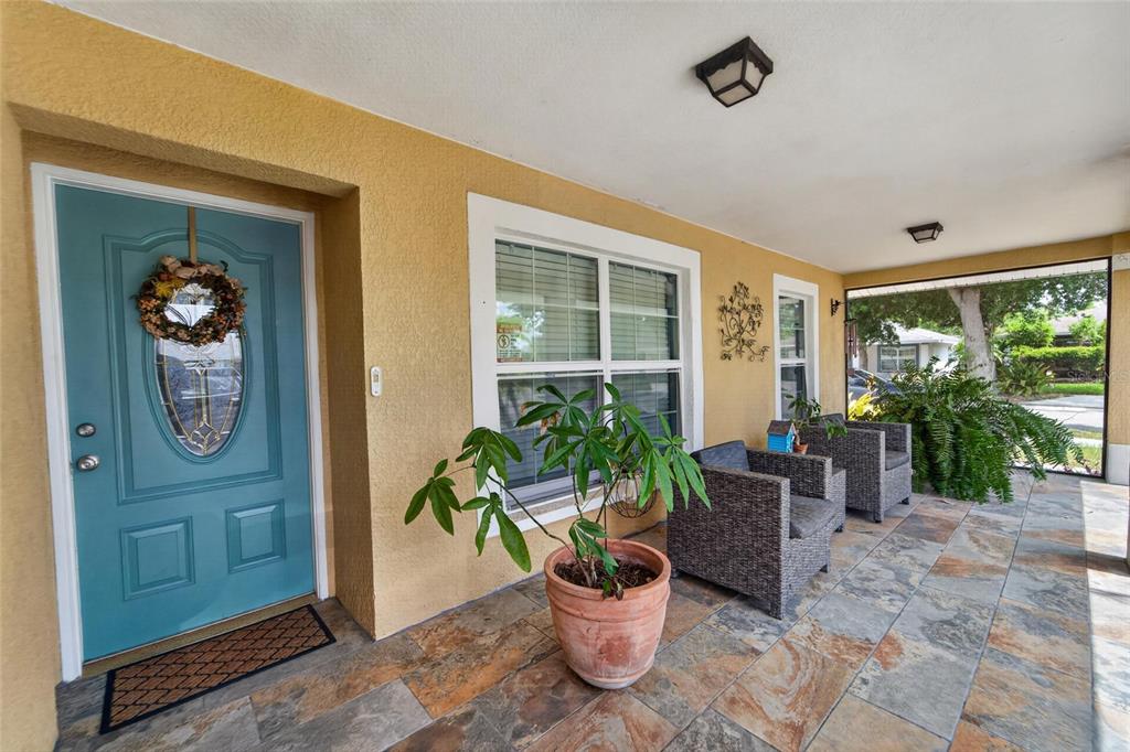 A covered front porch features tiled flooring, a teal front door, and two wicker chairs — 15428 FLORIDA BREEZE LOOP, WIMAUMA, FL