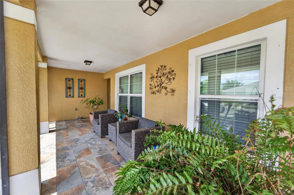 A covered front porch features tiled flooring, two wicker chairs, and decorative wall art — 15428 FLORIDA BREEZE LOOP, WIMAUMA, FL