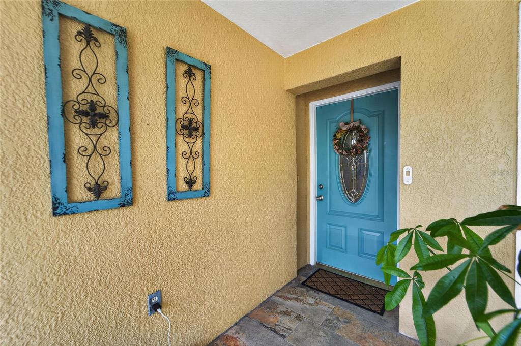 A teal front door with a wreath sits on a porch with yellow stucco walls — 15428 FLORIDA BREEZE LOOP, WIMAUMA, FL