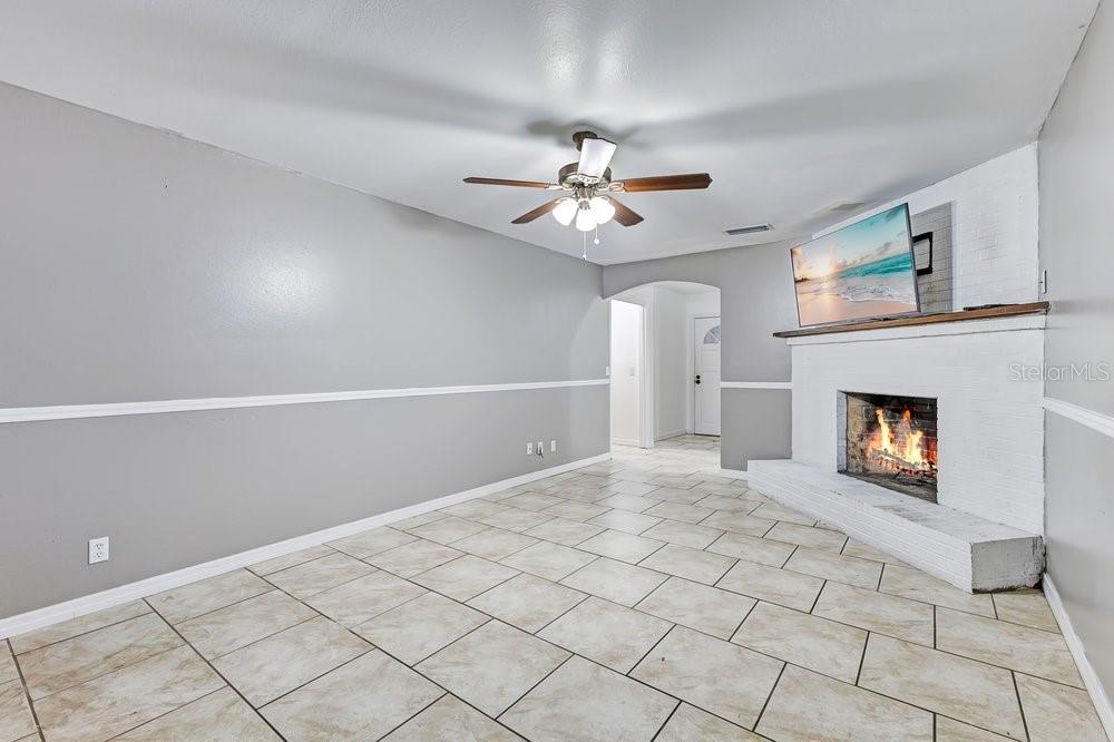 A living room with gray walls, tile flooring, a ceiling fan, and a white brick fireplace — 506 CLAYTON CIRCLE, WINTER HAVEN, FL