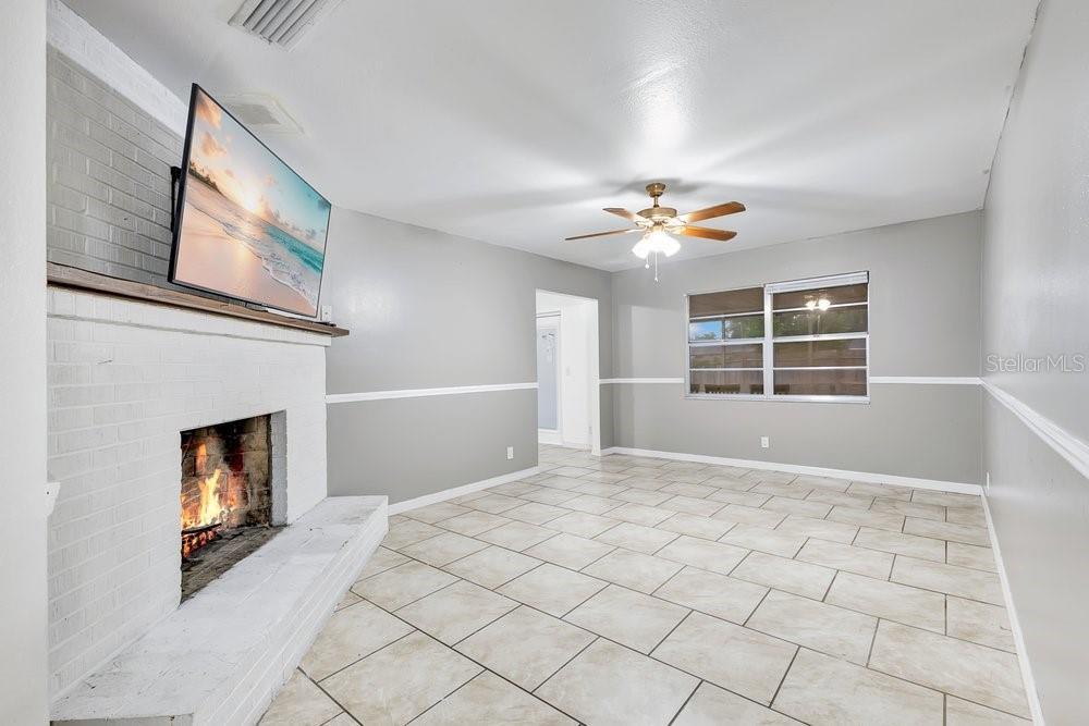 A living room with light tile floors, gray walls, a white brick fireplace, and ceiling fan — 506 CLAYTON CIRCLE, WINTER HAVEN, FL