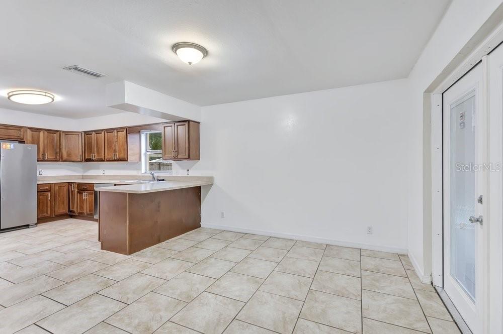 A kitchen with wood cabinets and tile flooring opens into a dining area with glass doors — 506 CLAYTON CIRCLE, WINTER HAVEN, FL