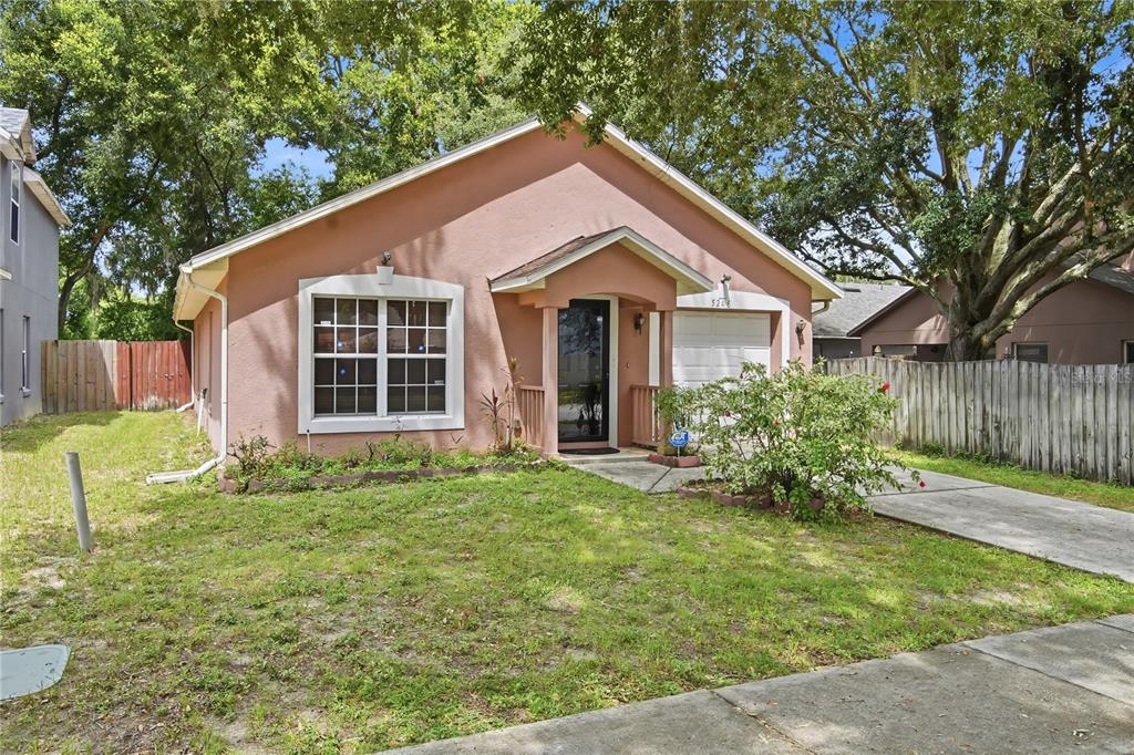 A single-story pink house with a front porch, garage, and a lawn under large trees — 5246 MANGO FRUIT STREET, SEFFNER, FL