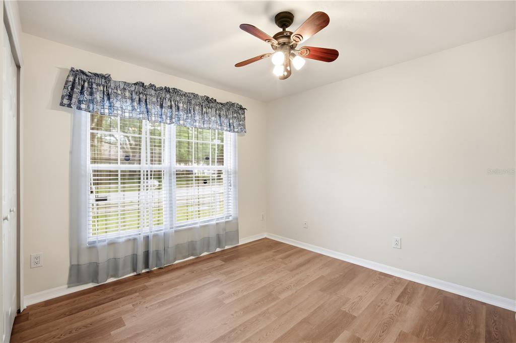 An empty bedroom features wood-look flooring, a ceiling fan, and a window with blue curtains — 5246 MANGO FRUIT STREET, SEFFNER, FL