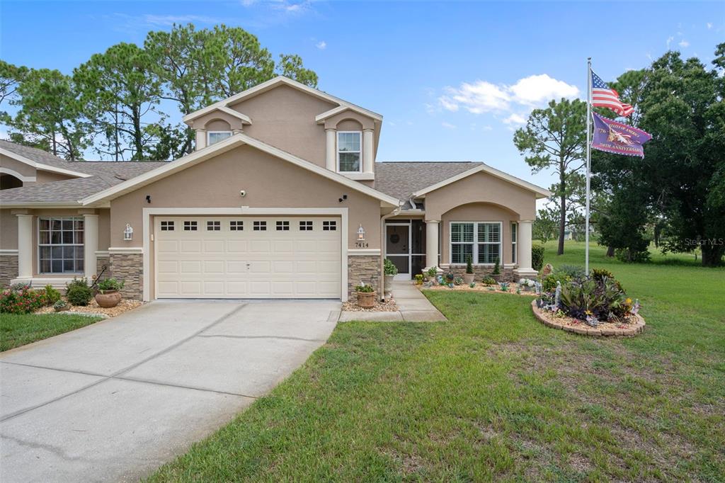 A tan stucco house with a two-car garage, a front porch, and a flag pole — 7414 MOORGATE COURT, NEW PORT RICHEY, FL