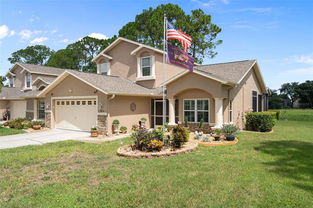 A two-story tan stucco house with a two-car garage and a front yard flagpole — 7414 MOORGATE COURT, NEW PORT RICHEY, FL