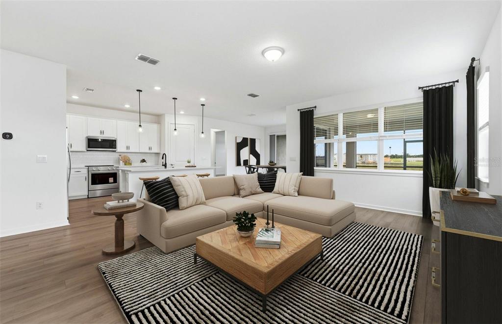 A modern open-concept living room features a beige sectional sofa, a wooden coffee table, and a kitchen — 10005 JOHNSON OAKS GLEN, PARRISH, FL