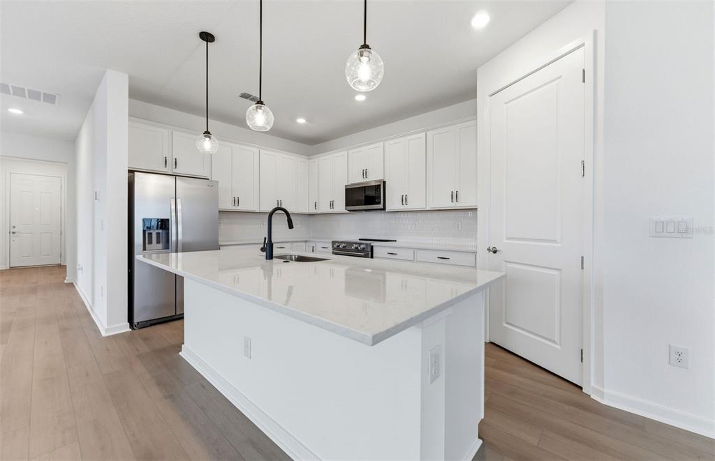 A modern kitchen features white cabinetry, a large island with a sink, and stainless appliances — 10005 JOHNSON OAKS GLEN, PARRISH, FL