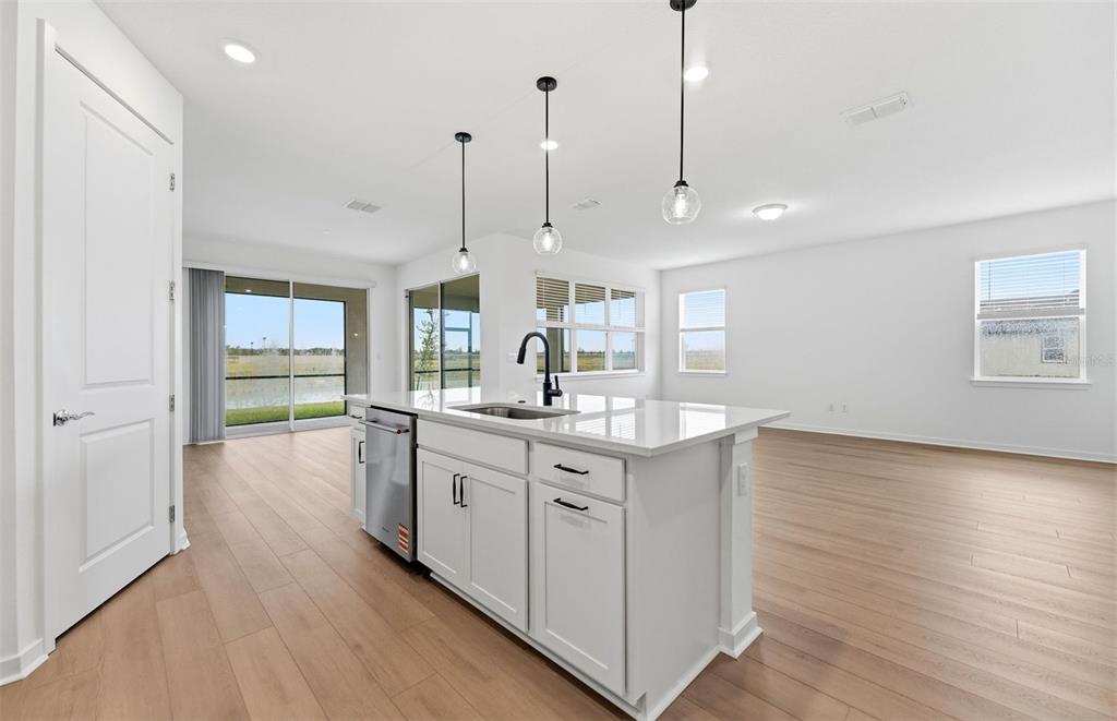 A kitchen island with a sink and dishwasher sits in a bright, open-concept living space — 10005 JOHNSON OAKS GLEN, PARRISH, FL