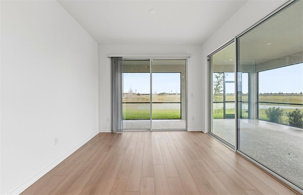 A bright room with light wood-look flooring, white walls, and sliding glass doors to a patio — 10005 JOHNSON OAKS GLEN, PARRISH, FL
