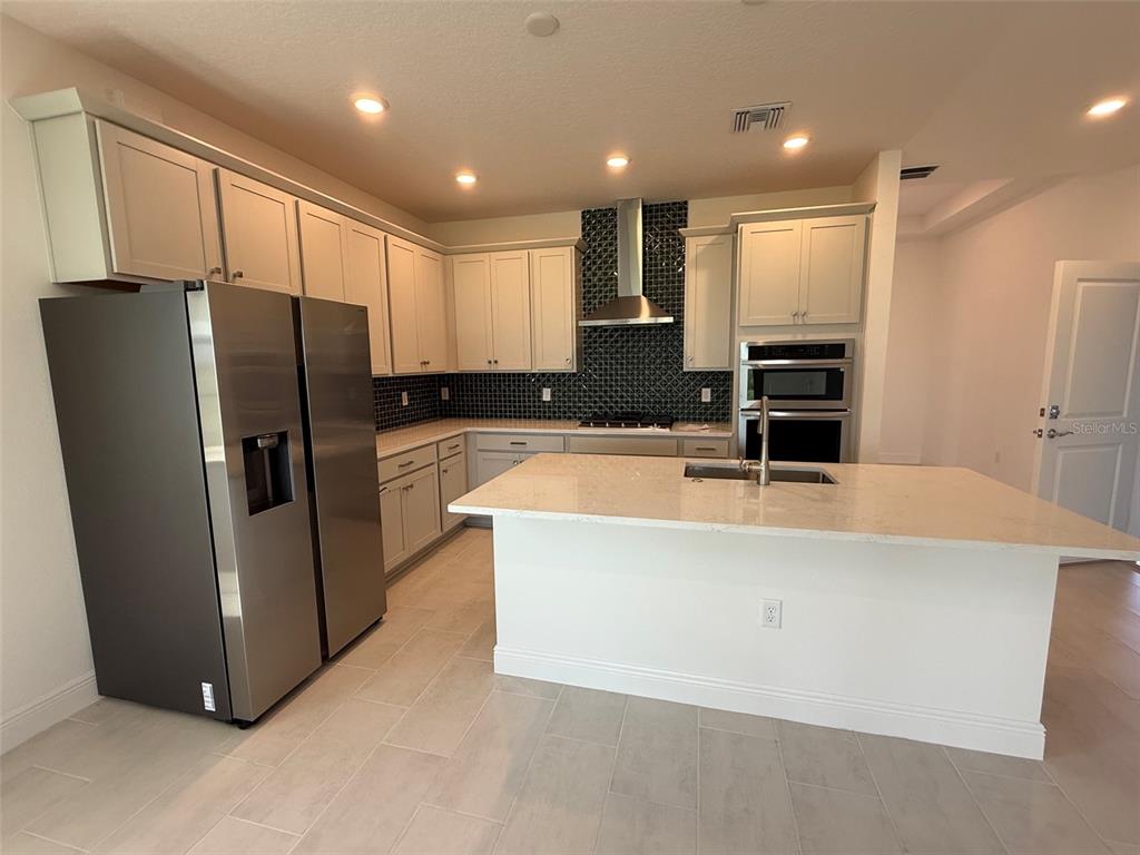 A kitchen features light-colored cabinetry, stainless steel appliances, a center island, and a tiled backsplash — 5127 BUTTONSAGE DRIVE, ST CLOUD, FL