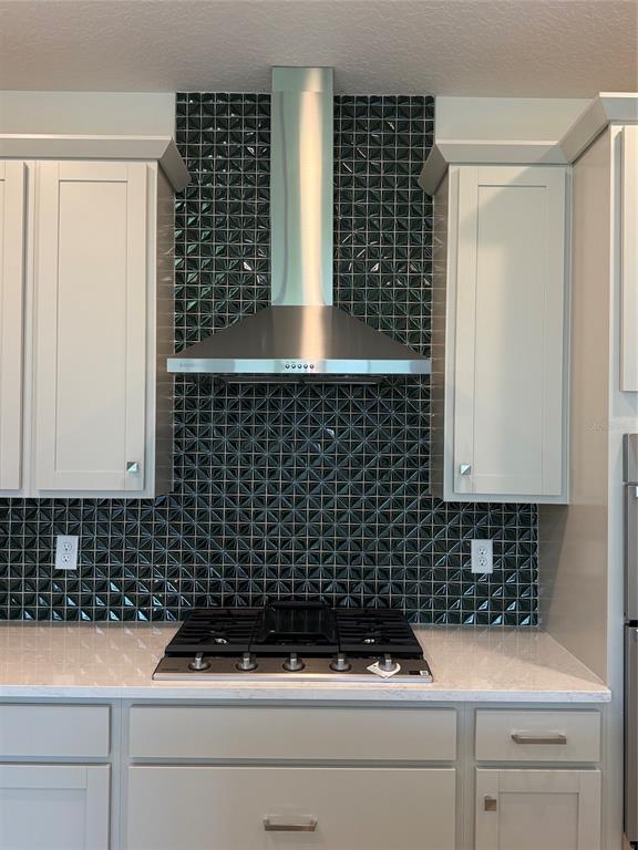 A kitchen features a stainless steel range hood, dark geometric backsplash tiles, and white cabinetry — 5127 BUTTONSAGE DRIVE, ST CLOUD, FL