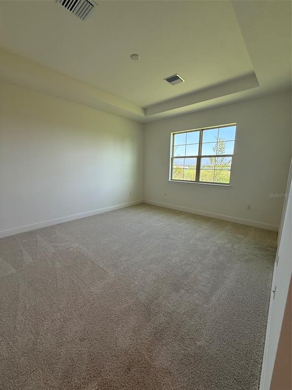 An empty bedroom features beige carpeting, white walls, and a tray ceiling with recessed lighting — 5127 BUTTONSAGE DRIVE, ST CLOUD, FL