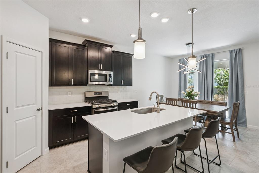 A kitchen features dark cabinets, a white island with bar stools, and a dining area — 1235 DORA PARC LANE, MOUNT DORA, FL