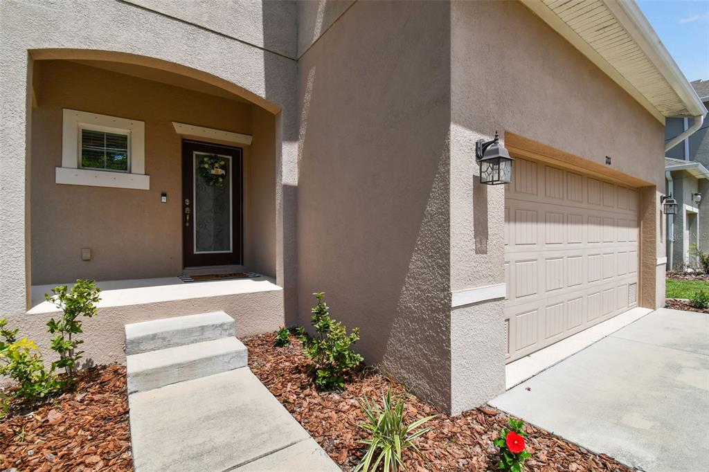 A beige stucco house exterior features a front entryway, a concrete walkway, and a garage — 7111 S WEST SHORE BOULEVARD, TAMPA, FL