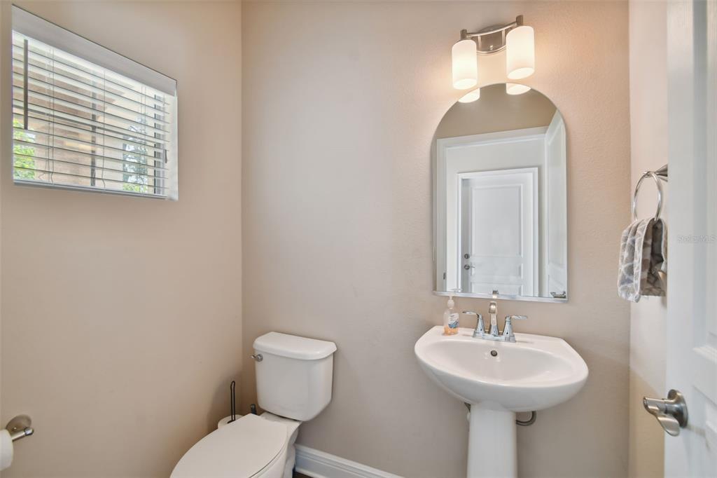 A powder room features a pedestal sink, a toilet, a mirror, and a window with blinds — 7111 S WEST SHORE BOULEVARD, TAMPA, FL