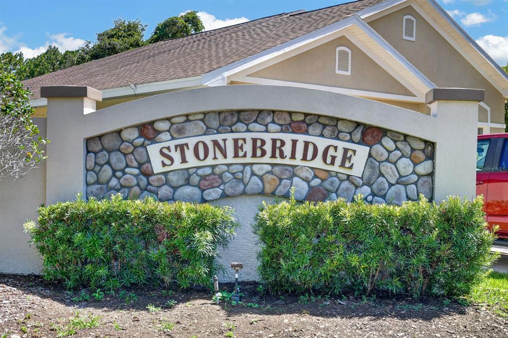 A stone-faced monument sign for Stonebridge stands in front of a tan building — 2322 STONEBRIDGE WAY, FLAGLER BEACH, FL