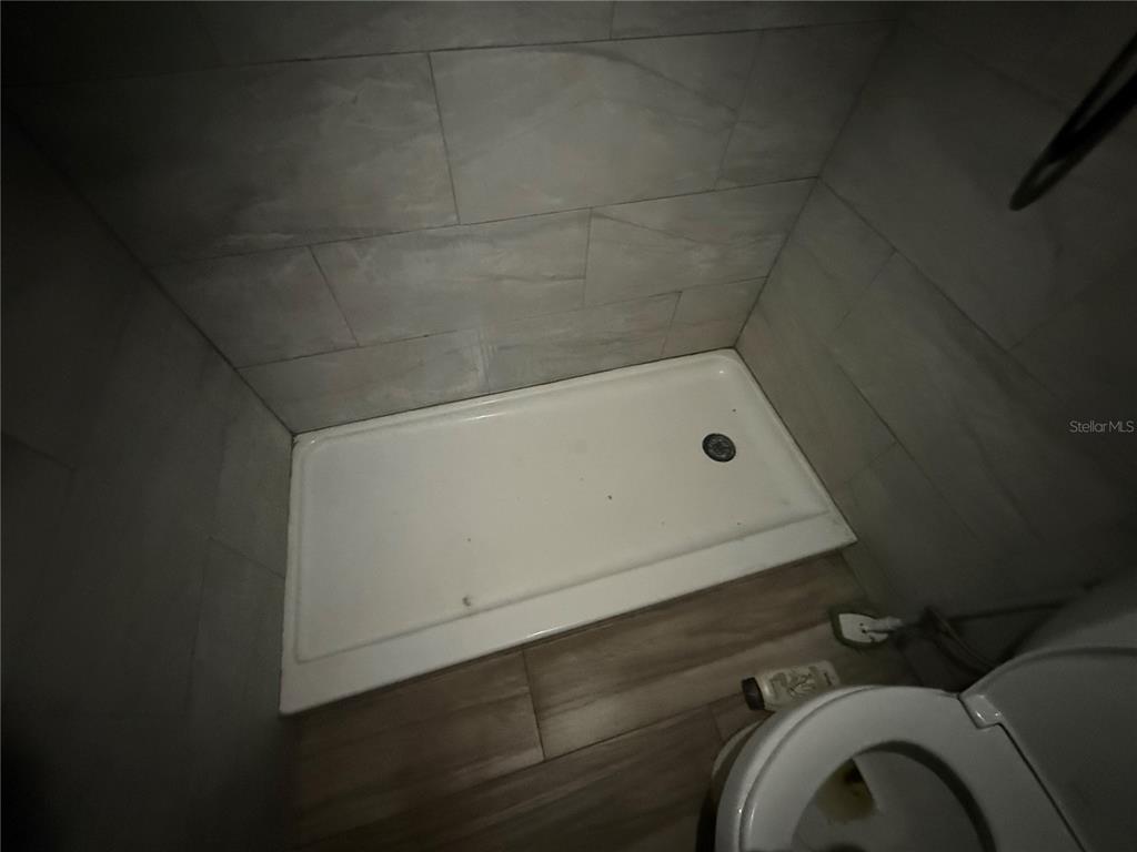 A white shower pan is installed in a tiled alcove next to a toilet — 10616 GODFREY LANE, ORLANDO, FL