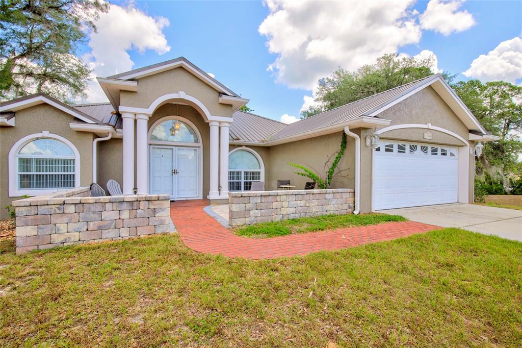 A single-story house with a tan stucco exterior, metal roof, and a brick walkway — 13059 NE 7TH LOOP, SILVER SPRINGS, FL