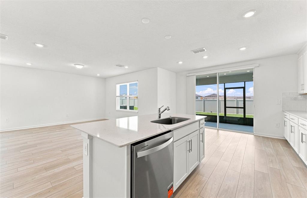 A modern kitchen features white cabinets, stainless steel appliances, quartz countertops, and light wood flooring — 1436 HAMILTON WAY, LAKE ALFRED, FL