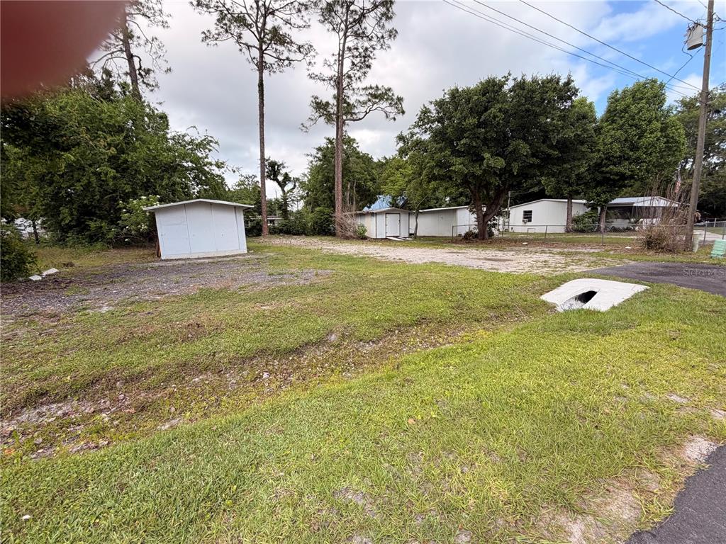 A grassy lot features a small white shed, gravel driveway, and nearby residential buildings — ARMADILLO ROAD, ASTOR, FL