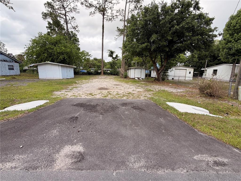 A paved driveway leads to a sandy lot with several small sheds and mature trees — ARMADILLO ROAD, ASTOR, FL