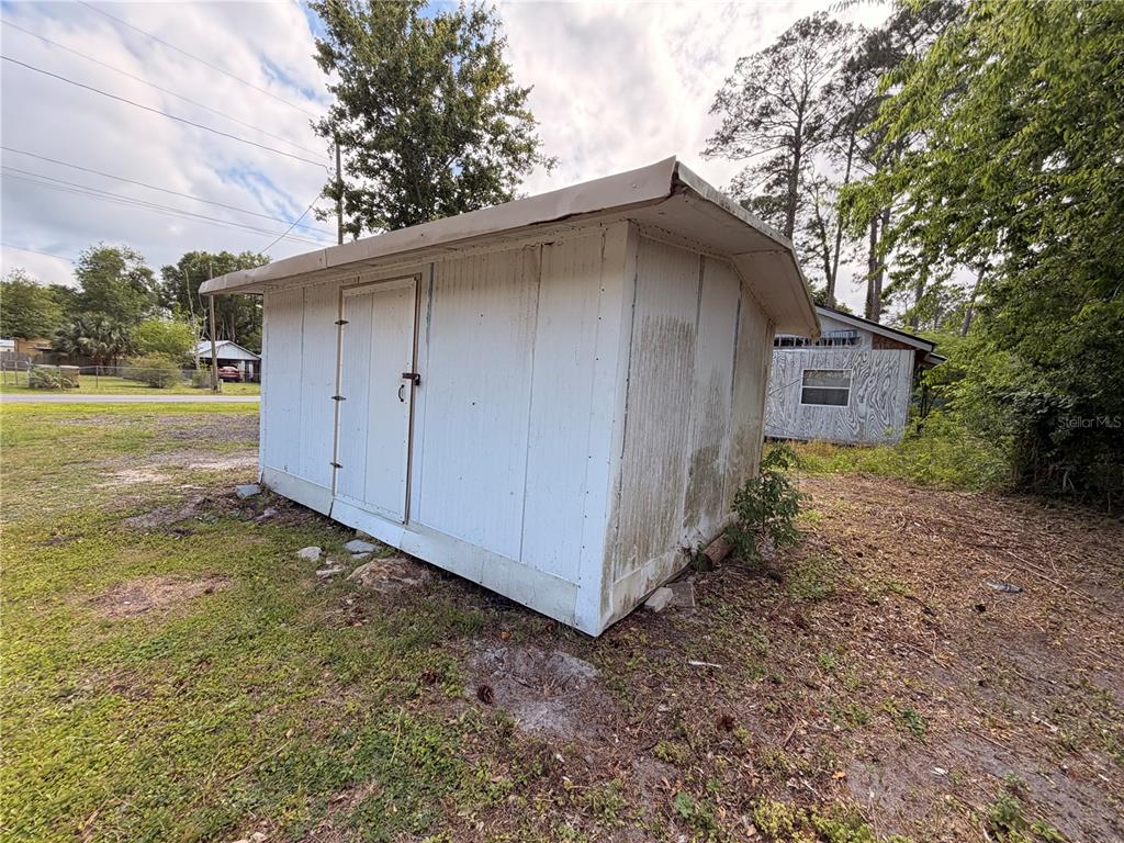 A weathered white shed sits on a grassy lot near a small house — ARMADILLO ROAD, ASTOR, FL