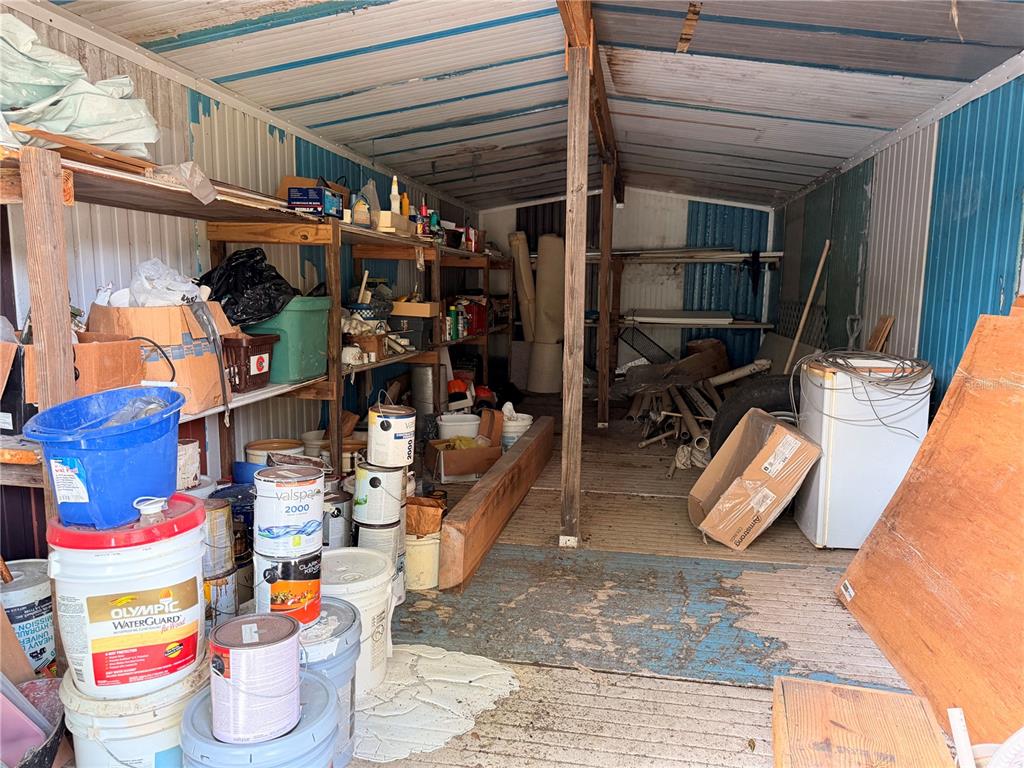 A cluttered storage shed features metal walls, wooden shelving units, and various containers and supplies — ARMADILLO ROAD, ASTOR, FL