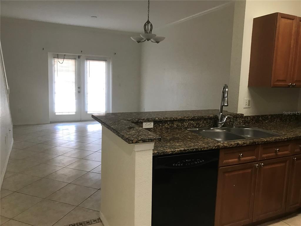 A kitchen with dark granite countertops and wood cabinets overlooks a tiled dining area — 2490 LANCIEN COURT UNIT 4, ORLANDO, FL