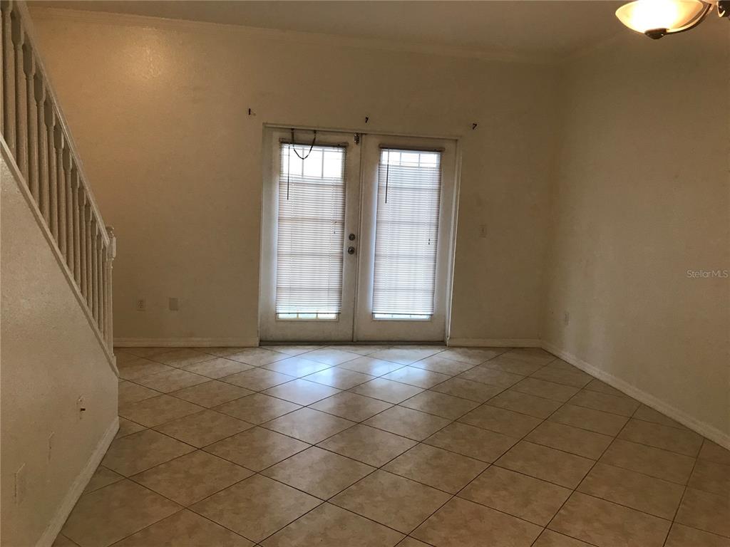 An empty room features beige tile flooring, a staircase with a white railing, and glass doors — 2490 LANCIEN COURT UNIT 4, ORLANDO, FL