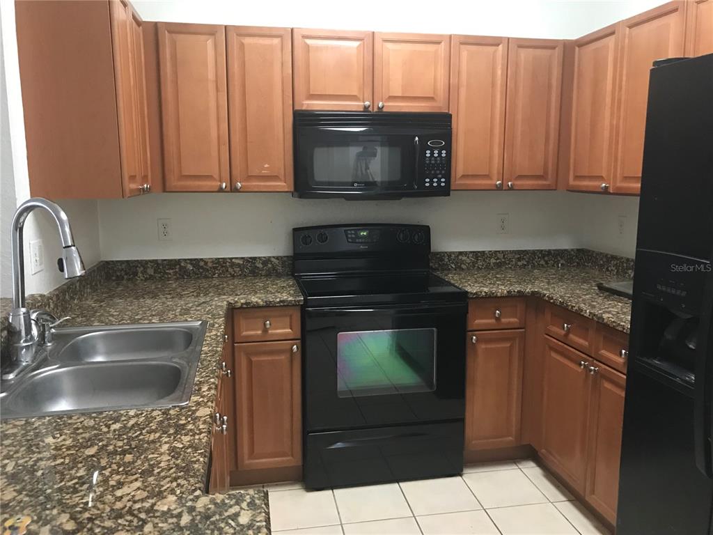 A kitchen features wood cabinets, granite countertops, black appliances, and a double-basin stainless steel sink — 2490 LANCIEN COURT UNIT 4, ORLANDO, FL