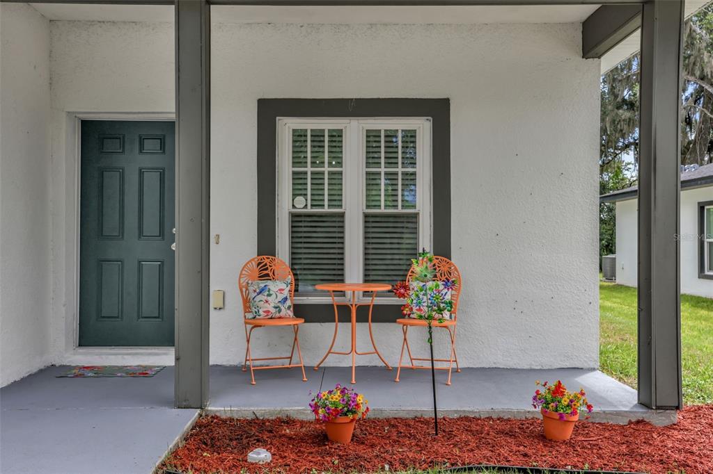A covered front porch features a dark door, a window, and two orange metal chairs — 430 W WALTS AVENUE, DELAND, FL