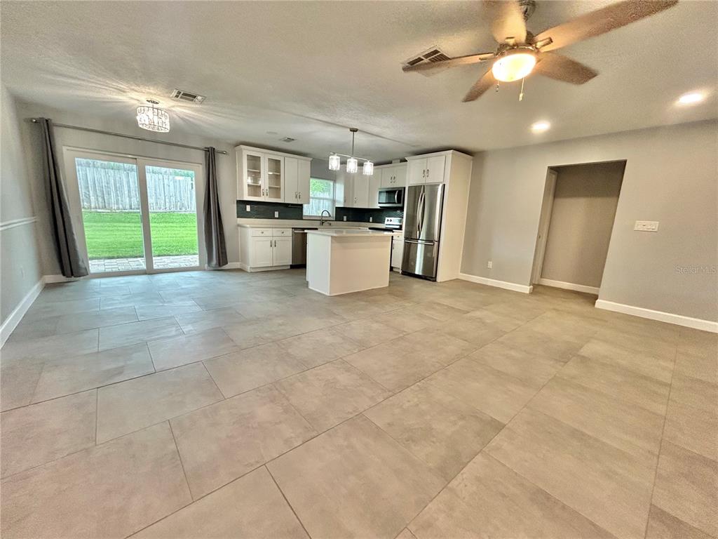 A kitchen with white cabinets, stainless steel appliances, and an island opens to a living area — 1444 OVERCASH DRIVE, DUNEDIN, FL
