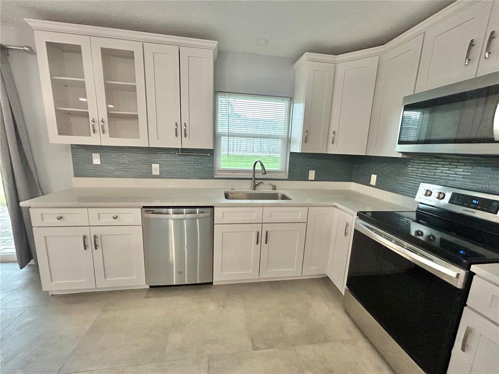 A kitchen with white cabinets, stainless steel appliances, and an island opens to a living area — 1444 OVERCASH DRIVE, DUNEDIN, FL
