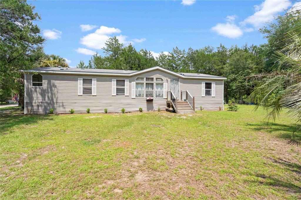 A single-story house with tan siding and a small wooden staircase leading to the entrance — 151 NE 164TH AVENUE, WILLISTON, FL