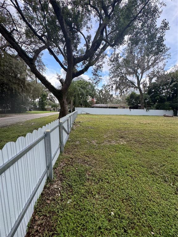 A white metal fence borders a grassy lot with large trees under a cloudy sky — KEUKA AVENUE, LEESBURG, FL