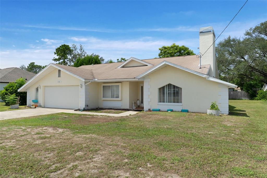 A single-story house with a beige exterior, a two-car garage, and a prominent chimney — 2501 MARINER BOULEVARD, SPRING HILL, FL